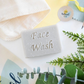 Facial soap bar (exfoliating) shown with greenery and a facecloth, the words 'Facial wash' stamped on the bar