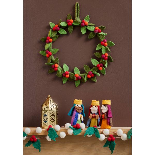 Felt berry wreath with green felt leaves and red felt berries, hanging on a wall with a felt nativity set
