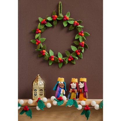 Felt berry wreath with green felt leaves and red felt berries, hanging on a wall with a felt nativity set