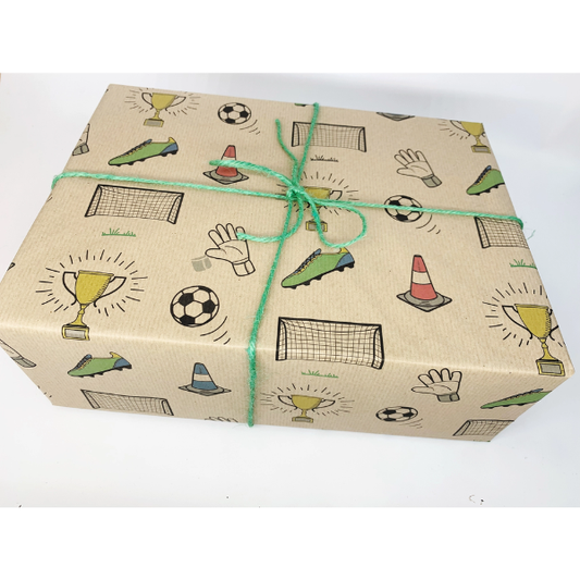 A rectangular gift box wrapped in brown kraft wrapping paper printed with football-themed illustrations including trophies, soccer balls, goals and a goalkeeper hand, tied with a green string on a white background.