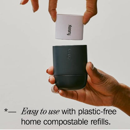 Hand putting a 'fussy' deodorant refill into its reusable container with text reading "Easy to use with plastic-free home compostable refills"