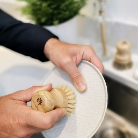 Person holding  a wooden 'geeky' pot brush with a spectacled face design washing a plate