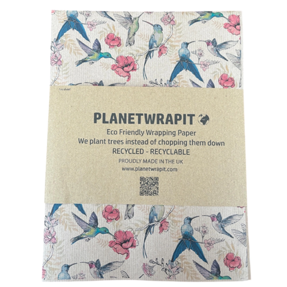 Planetwrapit eco-friendly wrapping paper folded and wrapped in a kraft paper band, featuring a pattern of blue hummingbirds, pink flowers, and green leaves on a brown kraft paper background.