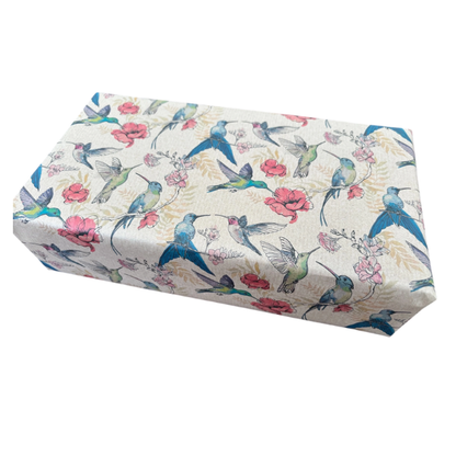 Planetwrapit eco-friendly wrapping paper shown on a wrapped parcel, featuring a pattern of blue hummingbirds, pink flowers, and green leaves on a brown kraft paper background.
