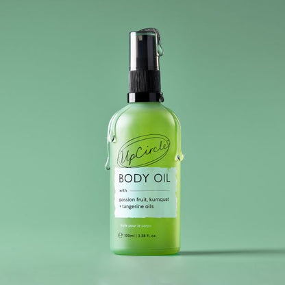 Green bottle of UpCircle body oil on a green background with drips of oil coming down the bottle