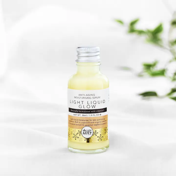 Bottle of Valley Mist Light Liquid Glow serum with aluminium cap on a white background with greenery.