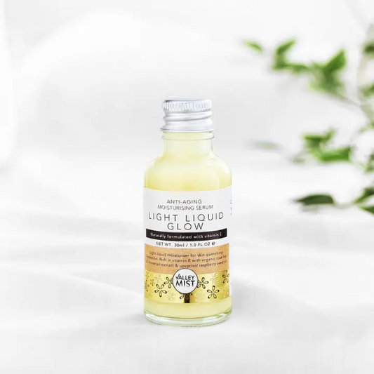 Bottle of Valley Mist Light Liquid Glow serum with aluminium cap on a white background with greenery.