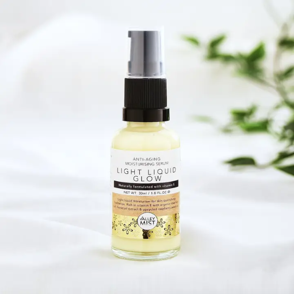 Bottle of Valley Mist Light Liquid Glow serum with pump on a white background with greenery.