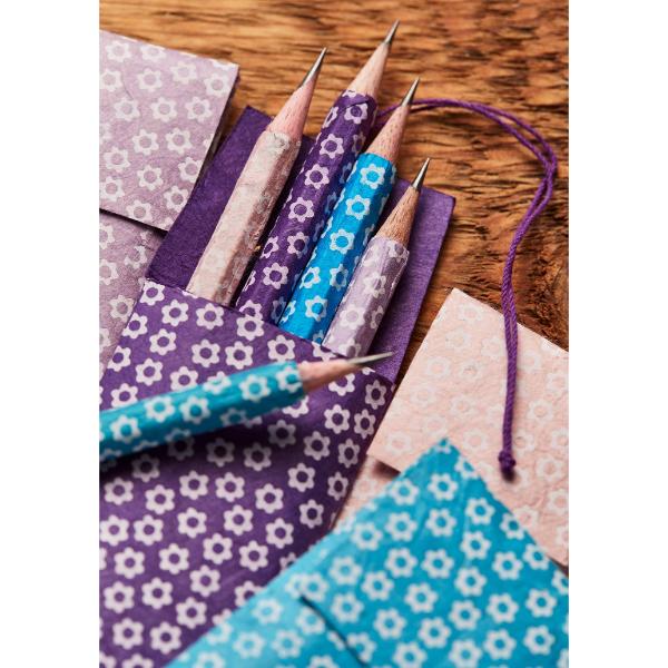 A close-up of patterned pencil paper cases holding several pencils on a wooden surface. The cases have white floral motifs on purple and turquoise backgrounds, with matching fabric tags and drawstring cords.