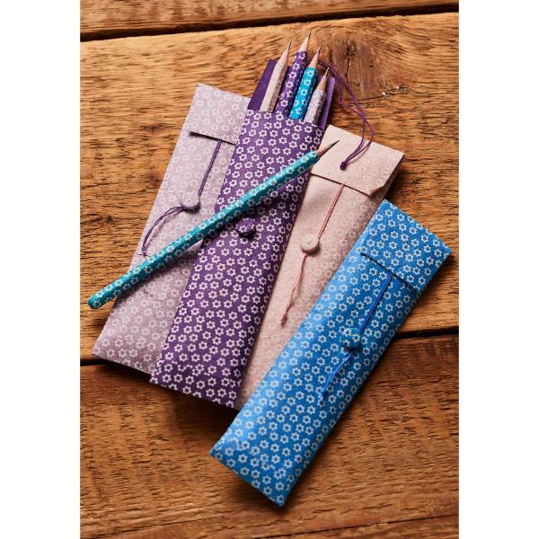 Three paper pencil cases in light purple, pink, and blue with a white floral pattern, shown on a rustic wooden table with pencils inside.