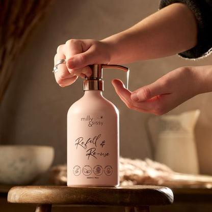 Refillable aluminium bottle in blush pink with a hand  pressing the pump with product coming out