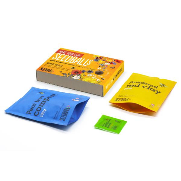Seedball kit with packaging, coloured powders, and labels on a white background