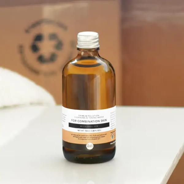 Men's micellar water and toner in dark brown glass bottle with aluminium lid on a white surface with cardboard in background