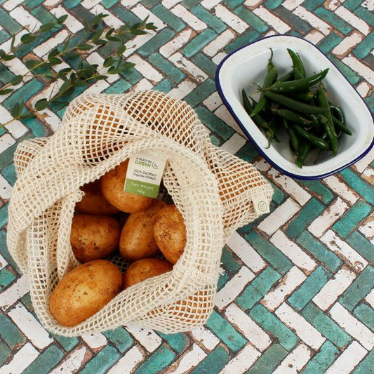 Mesh bag of potatoes next to a bowl of green beans on a patterned table