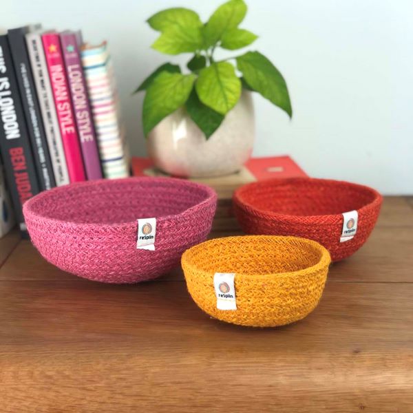 Set of three mini jute bowls in Fire colour (bright pink, orange and yellow)  sitting on a wooden tabletop