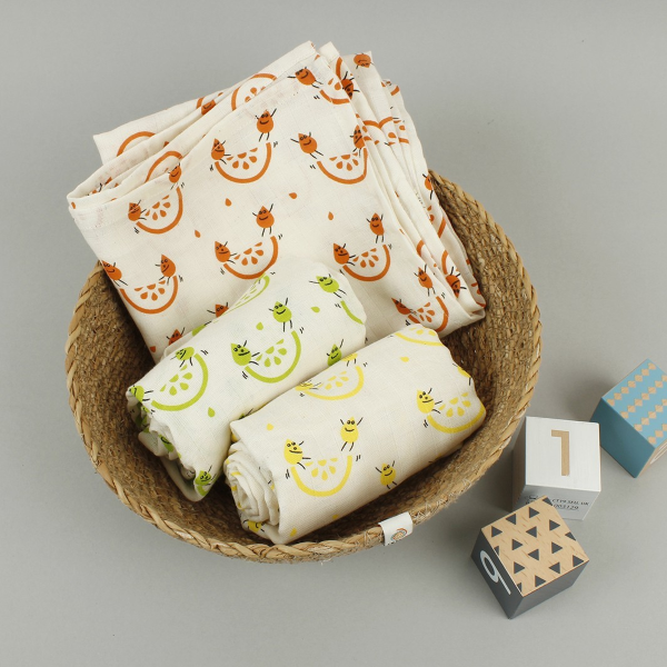 Organic cotton set of three muslin cloths, shown inside a basket with wooden child's blocks alongside.  All with cream background with colourful fruity images.