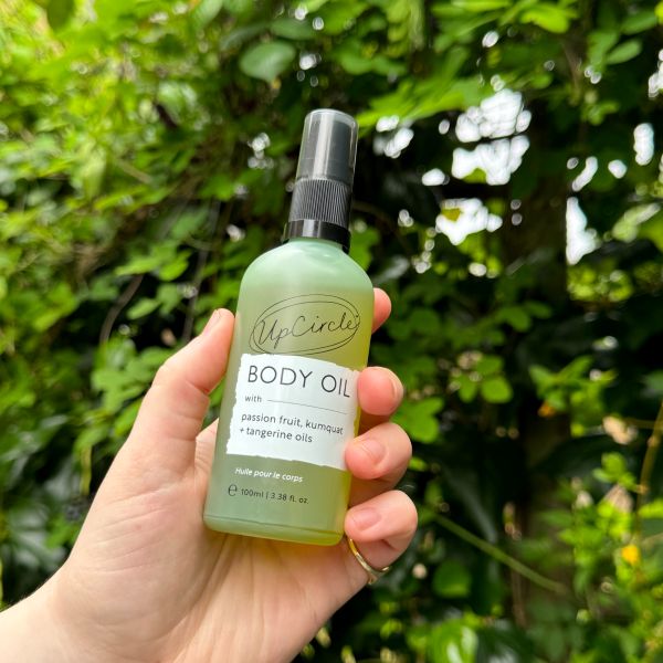 Hand holding a bottle of UpCircle's Body Oil with trees in the background