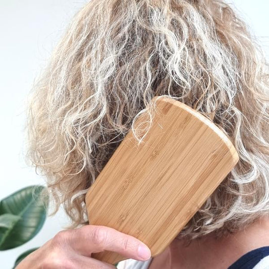 Person using wooden paddle hairbrush on their hair with a blurred background