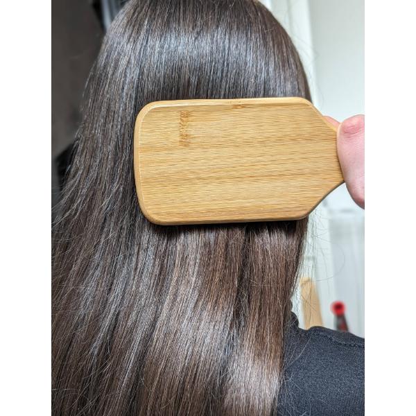 Person using a wooden paddle hairbrush comb on their long hair