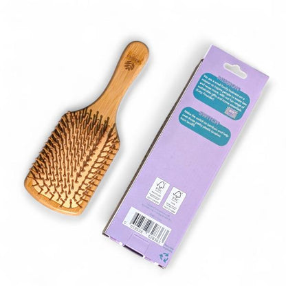 Wooden bamboo paddle hairbrush next to its cardboard packaging on a white background