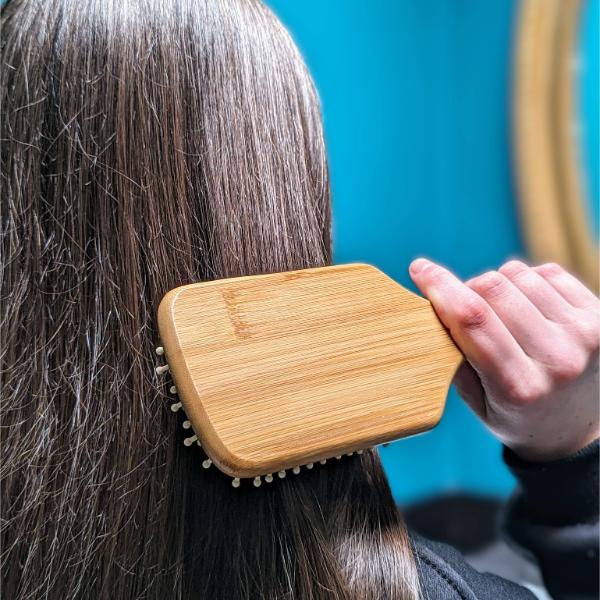Person using wooden bamboo hairbrush on their hair against a blue background