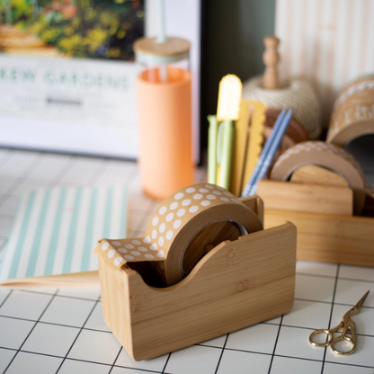 Bamboo tape dispenser with brown polka dot tape on a desk with stationery items.