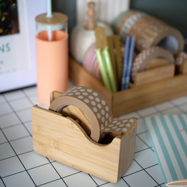 Bamboo tape dispenser with polka dot tape on a desk with stationery items.