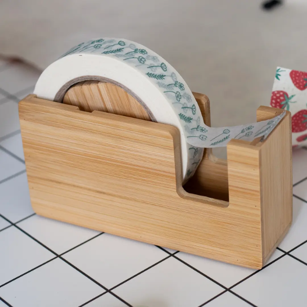 Bamboo tape dispenser with a roll of white floral paper tape on a craft table
