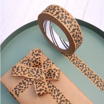 Roll of brown paper tape with black animal print design shown on the roll and applied to a brown paper wrapped gift 