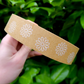 Roll of brown paper tape with white flower design held in a hand with a leafy background