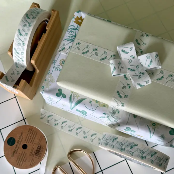 White paper tape with green floral design shown on the roll in a bamboo dispenser and applied to a wrapped gift