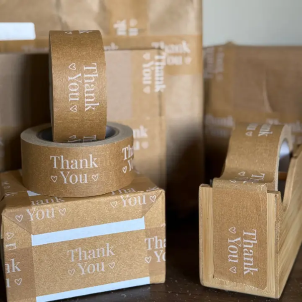 Brown paper tape with 'Thank You' text on bamboo paper tape dispenser and boxes.
