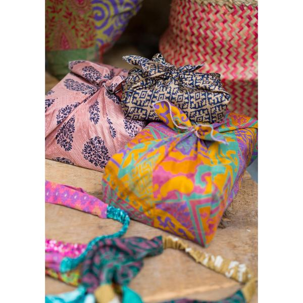 Three colourful fabric wrapped gift , displayed on a rustic wooden surface with other patterned textiles in the background.