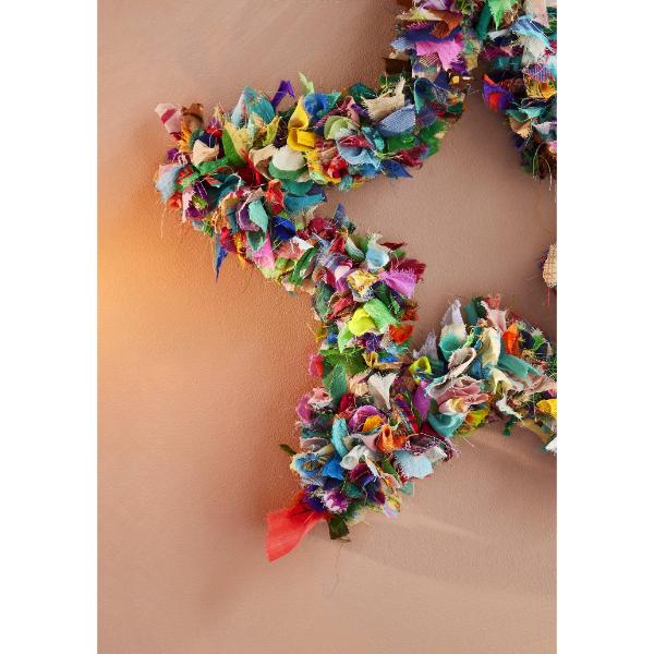 Recycled sari wreath using multicoloured sari remnants, shaped into a star design shown close up hanging on a wall.