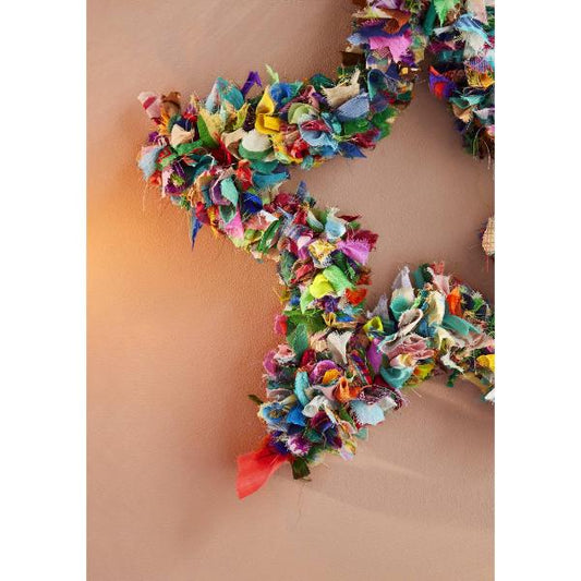 Recycled sari wreath using multicoloured sari remnants, shaped into a star design shown close up hanging on a wall.