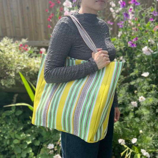 Recycled cement sack in 'Beach' colourway (yellow, white, green stripes) shown in use on somebody's shoulder