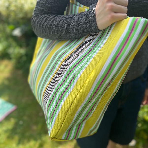 Recycled cement sack in 'Beach' colourway (yellow, white, green stripes) shown in use on somebody's shoulder