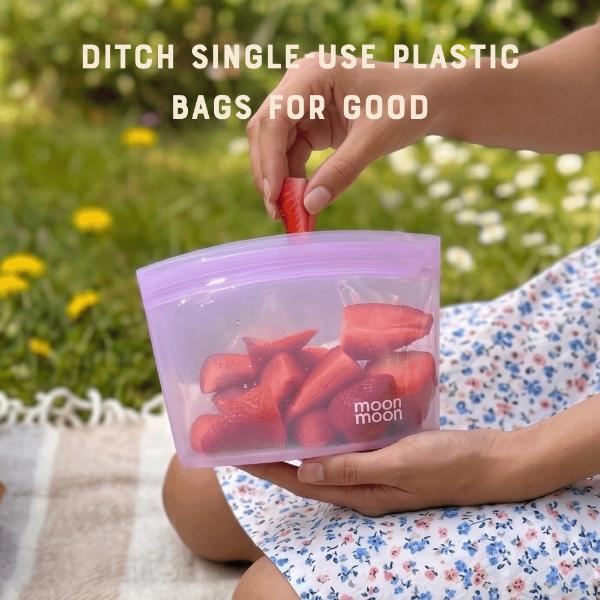 Person holding a reusable silicone food bag with strawberries inside, outdoors, with text reading "Ditch single use plastic bags for good"