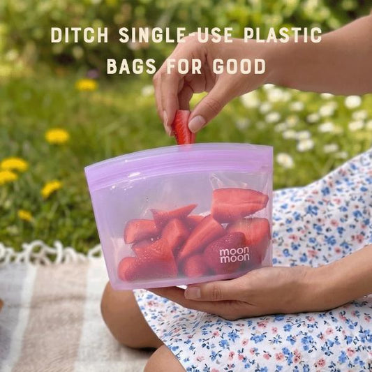 Person holding a reusable silicone food bag with strawberries inside, outdoors, with text reading "Ditch single use plastic bags for good"