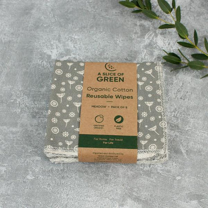A pack of reusable wipes on a textured grey surface with green leaves in the corner. 