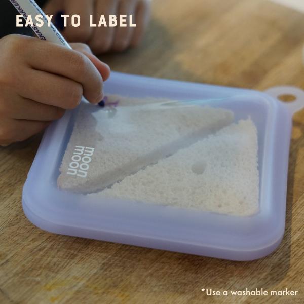 Person writing on a purple silicone sandwich case with a sandwich inside