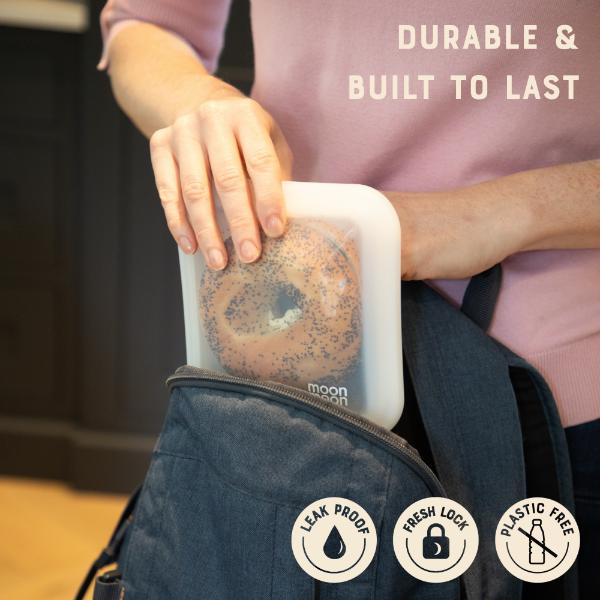 Person holding a silicone sandwich case with a bagel inside, with text reading "Durable and built to last" and logos reading Leak proof, fresh lock and plastic-free