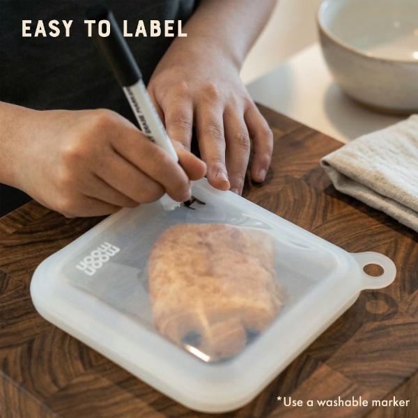 Person labelling silicone sandwich case storage bag with a marker on a wooden table and text reading "Easy to label"