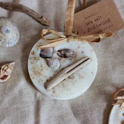 Scented home decoration in 'beach and coastal' scent, wax melt with shells and driftwood embedded in the wax, with a raffia hanging loop and paper label