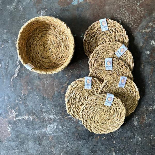 Set of 6 natural seagrass coasters with a holder, laid on a dark grey marble background