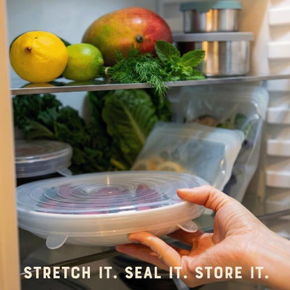 Hand holding a silicone lid on a bowl with fruits and vegetables, with text 'Stretch it. Seal it. Store it.'