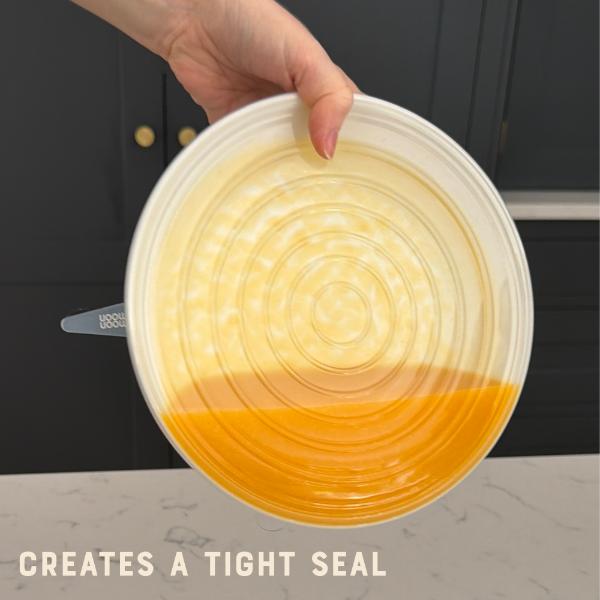 Hand holding a bowl containing liquid but sealed with a silicone lid surface sideways with text 'CREATES A TIGHT SEAL'.