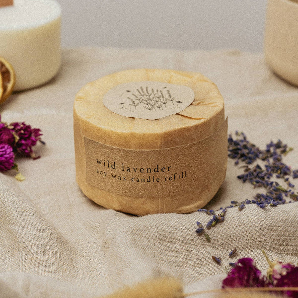 Candle refill container labeled 'wild lavender' on a textured surface with dried lavender flowers.