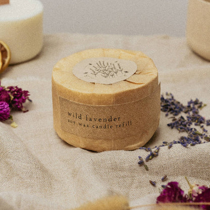 Candle refill container labeled 'wild lavender' on a textured surface with dried lavender flowers.