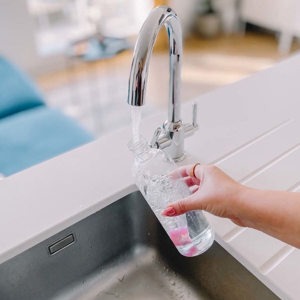 Mack spray bottle with pod inside being filled with water at a sink 